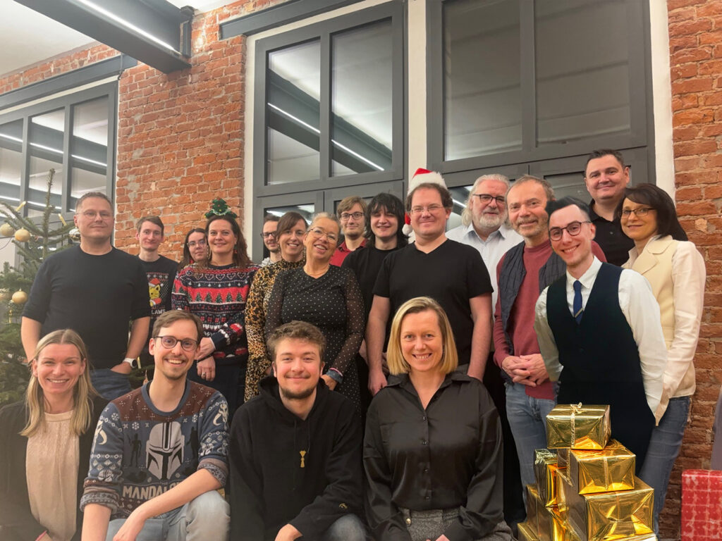 Gruppenbild von 19 Personen auf der firmeninternen Weihnachtsfeier, alle lächeln in die Kamera